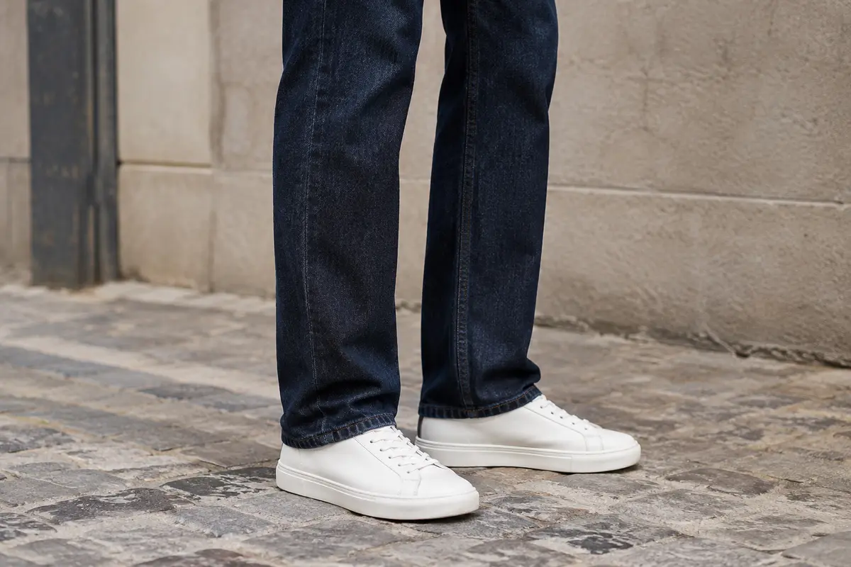 Pantalon droit bleu foncé dont l’ourlet effleure une paire de baskets basses blanches.