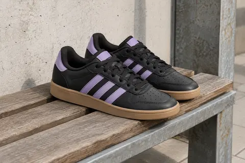 Baskets Adidas Breaknet Sleek noires et lilas posées sur un banc en bois près d’un mur de béton clair.
