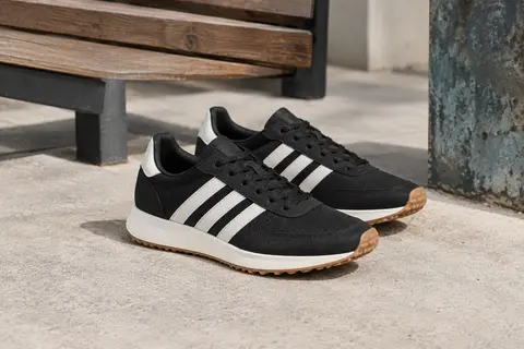 Baskets Adidas Run 70S 2.0 noires et blanches à tige basse, posées sur du béton clair près d’un banc en bois.