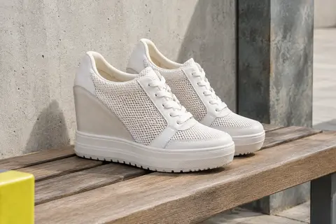 Baskets compensées blanches en filet, à lacets, photographiées sur un banc en bois en décor urbain