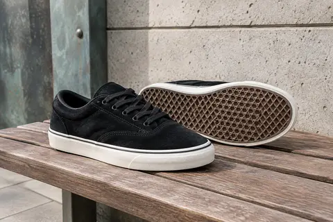 Baskets de skate basses en suède noir, posées sur un banc en bois dans un décor urbain.