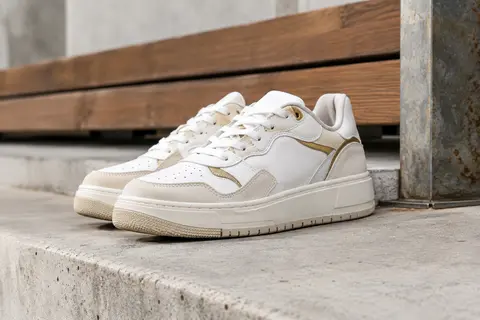 Baskets Puma Caven III basses, blanches avec détails dorés, posées sur un socle de béton clair.