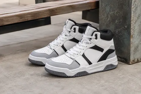 Baskets Puma Rebound V6 mi-hautes blanches, noires et grises, posées sur du béton près d’un banc en bois.