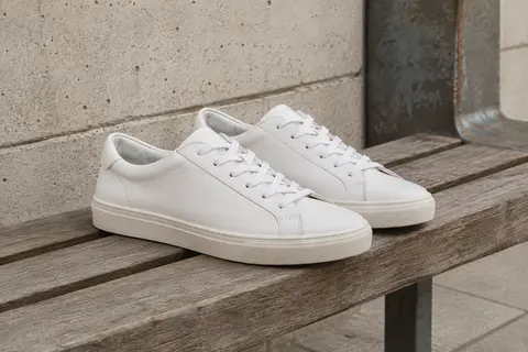 Baskets basses blanches en cuir Puma Smash Wns v2 L posées sur un banc en bois dans un décor urbain.
