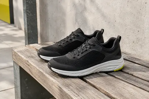 Paire de sneakers basses noires Skechers avec finition mesh, posées sur un banc en bois en décor urbain.
