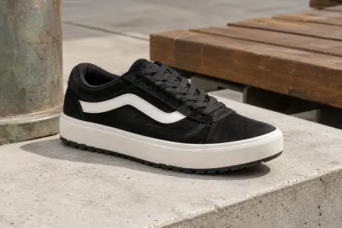 Basket basse Vans Range EXP noire et blanche en daim, posée sur un socle de béton clair